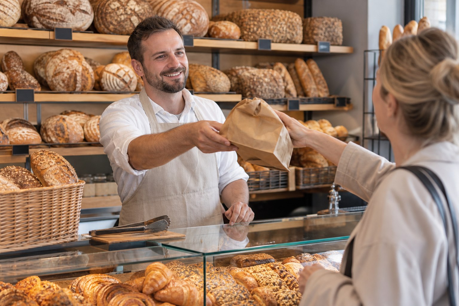 Bäckereifachverkäufer bedient eine Kundin an der Verkaufstheke